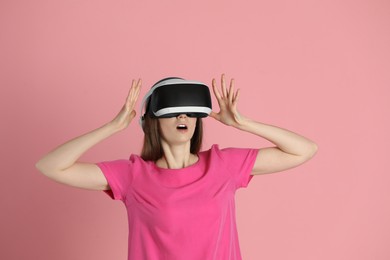 Surprised woman using virtual reality headset on pink background