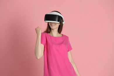 Photo of Smiling woman using virtual reality headset on pink background