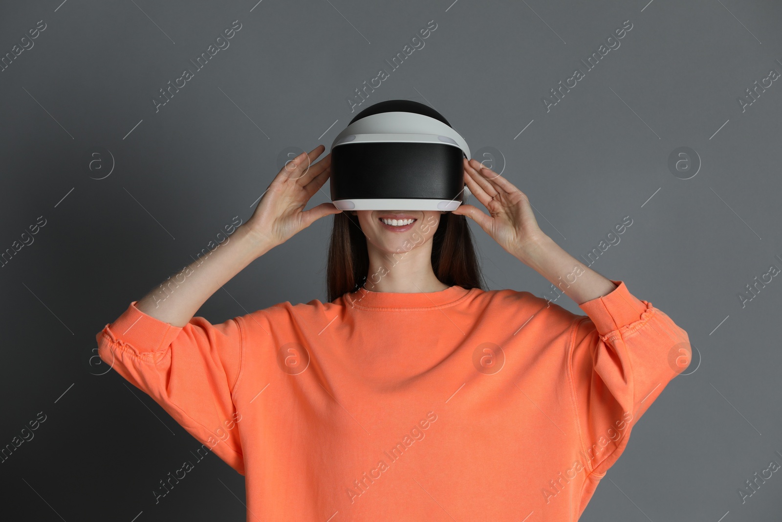 Photo of Smiling woman using virtual reality headset on gray background