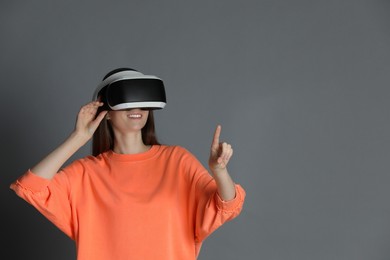 Photo of Smiling woman using virtual reality headset on gray background, space for text