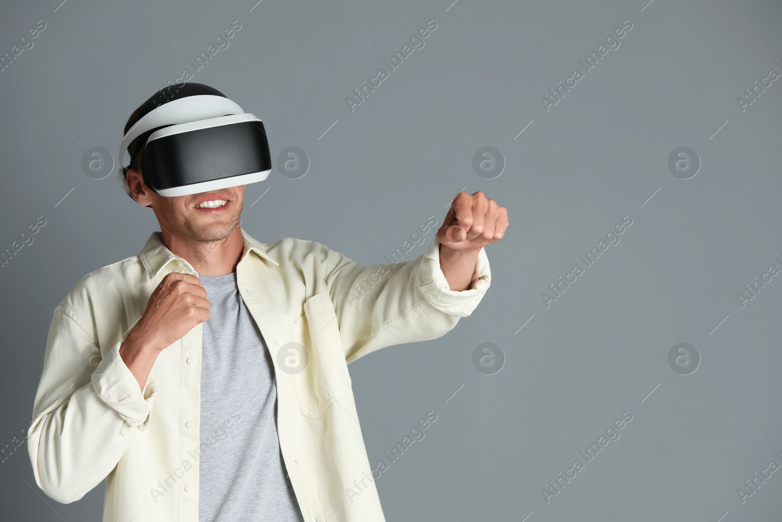 Photo of Smiling man using virtual reality headset on gray background, space for text