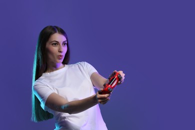 Excited woman playing video games with controller on violet background, space for text