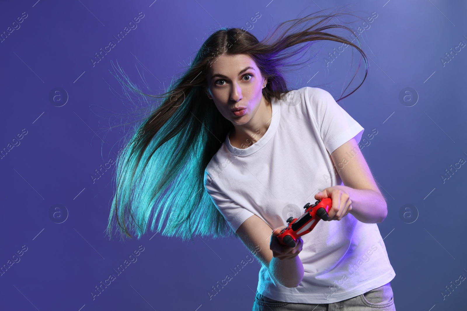 Photo of Surprised woman playing video games with controller on violet background