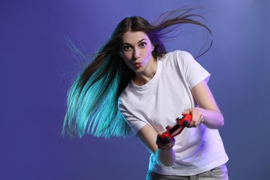 Surprised woman playing video games with controller on violet background