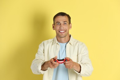 Happy man playing video games with controller on yellow background