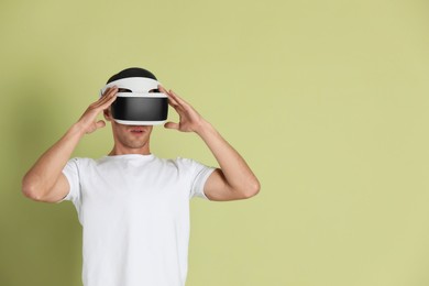 Photo of Surprised man using virtual reality headset on light green background, space for text