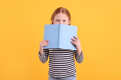 Photo of Cute little girl with book on yellow background