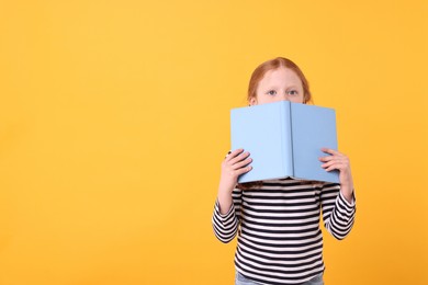 Photo of Cute little girl with book on yellow background. Space for text