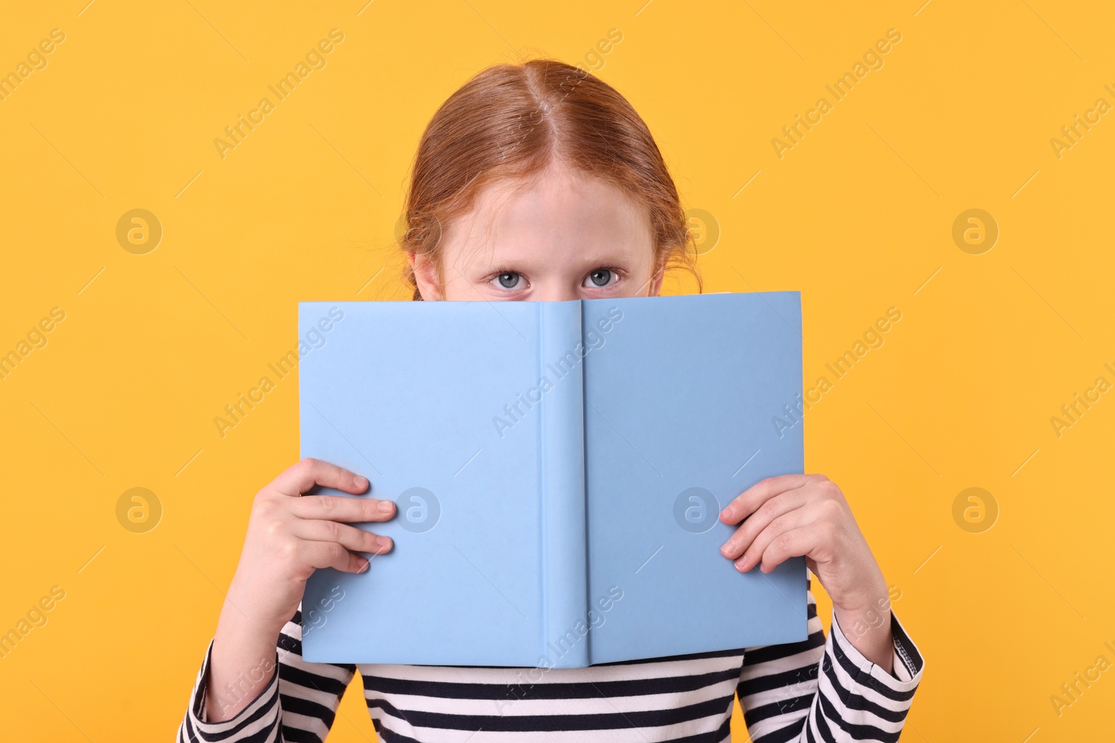 Photo of Cute little girl with book on yellow background