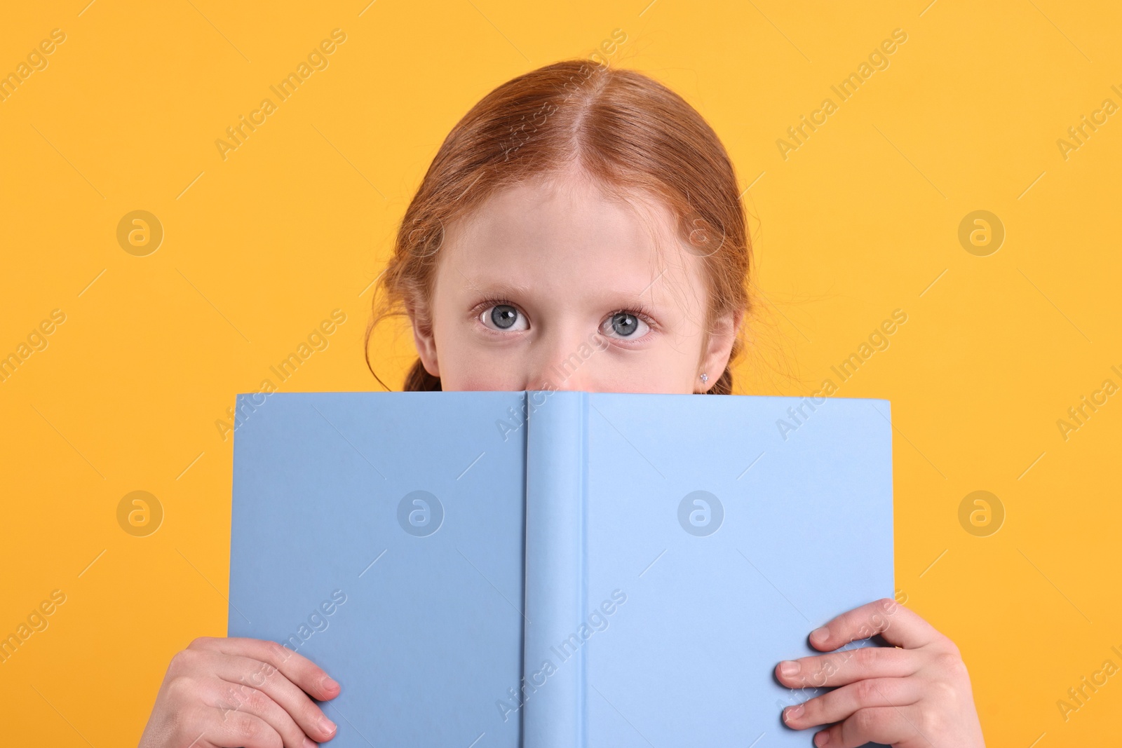 Photo of Cute little girl with book on yellow background