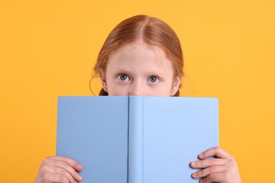 Cute little girl with book on yellow background