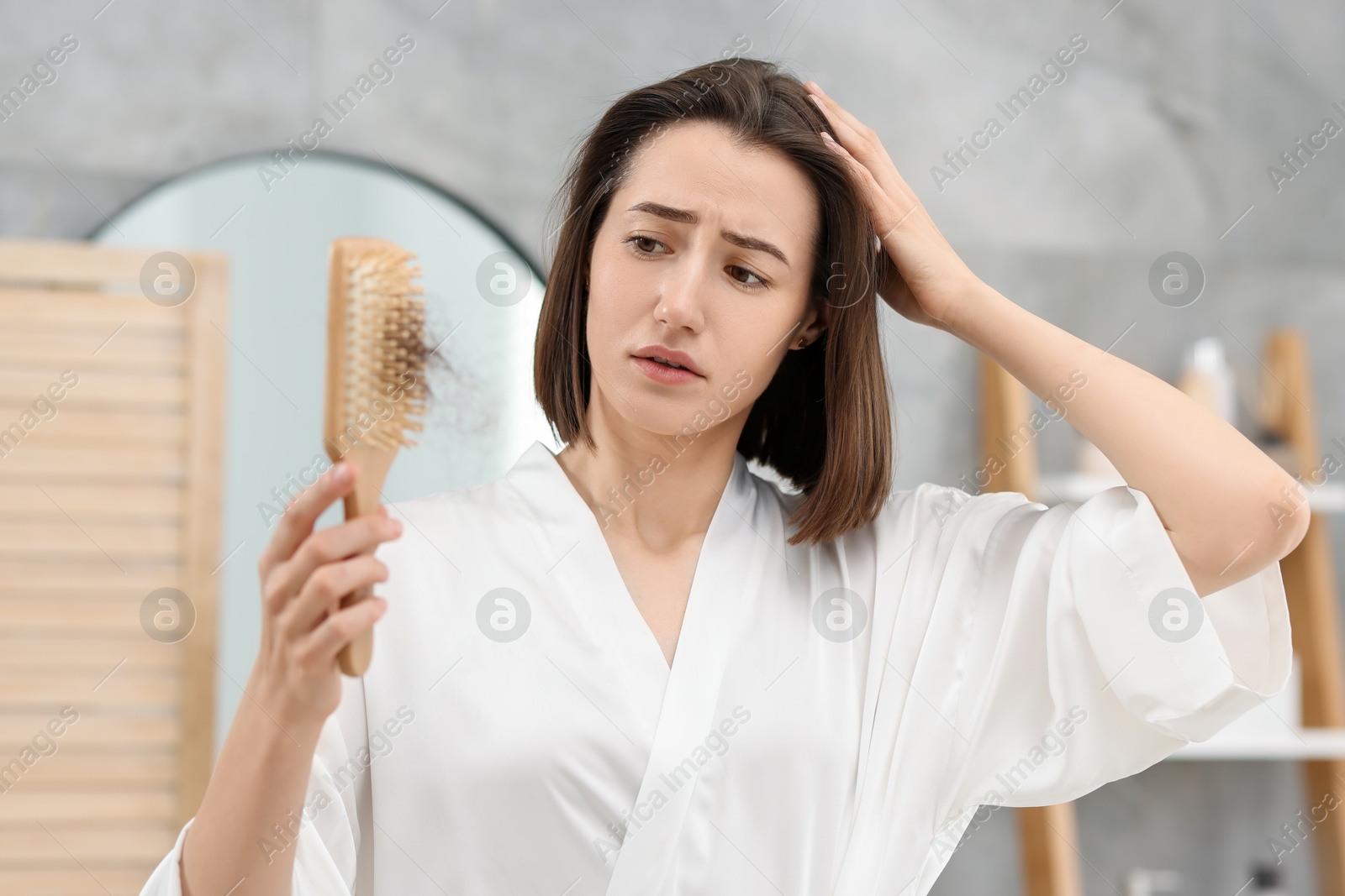 Photo of Sad woman holding brush with lost hair in bathroom. Alopecia problem