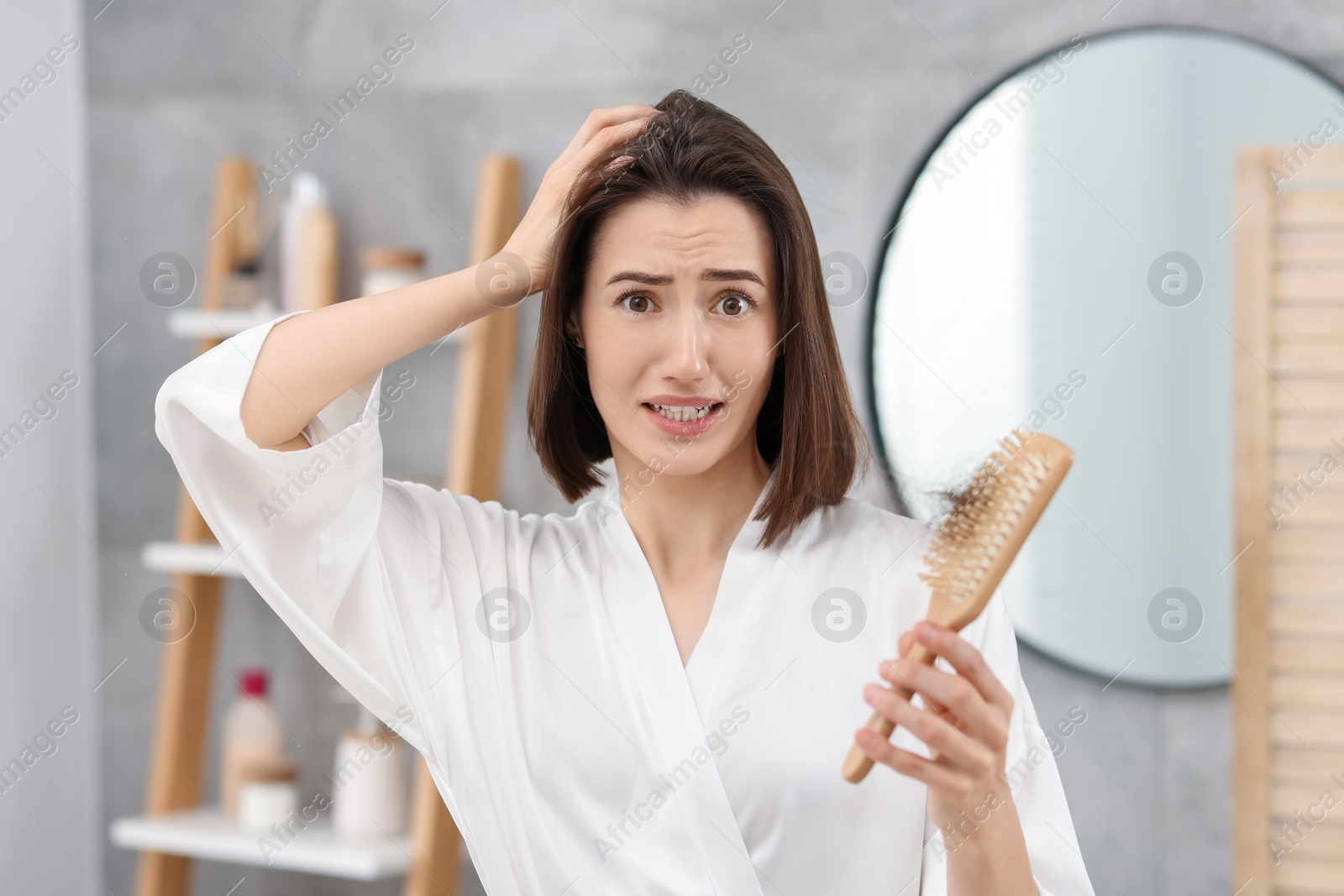 Photo of Emotional woman holding brush with lost hair in bathroom. Alopecia problem