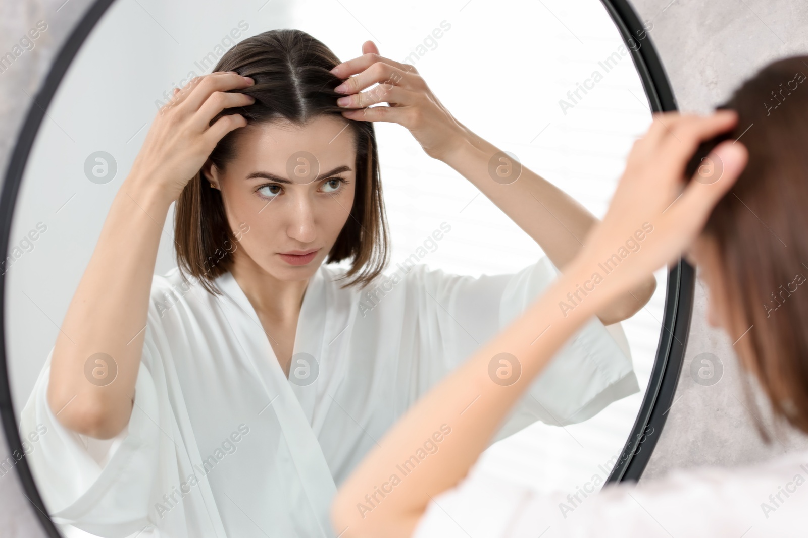 Photo of Young woman with hair loss problem looking at mirror indoors