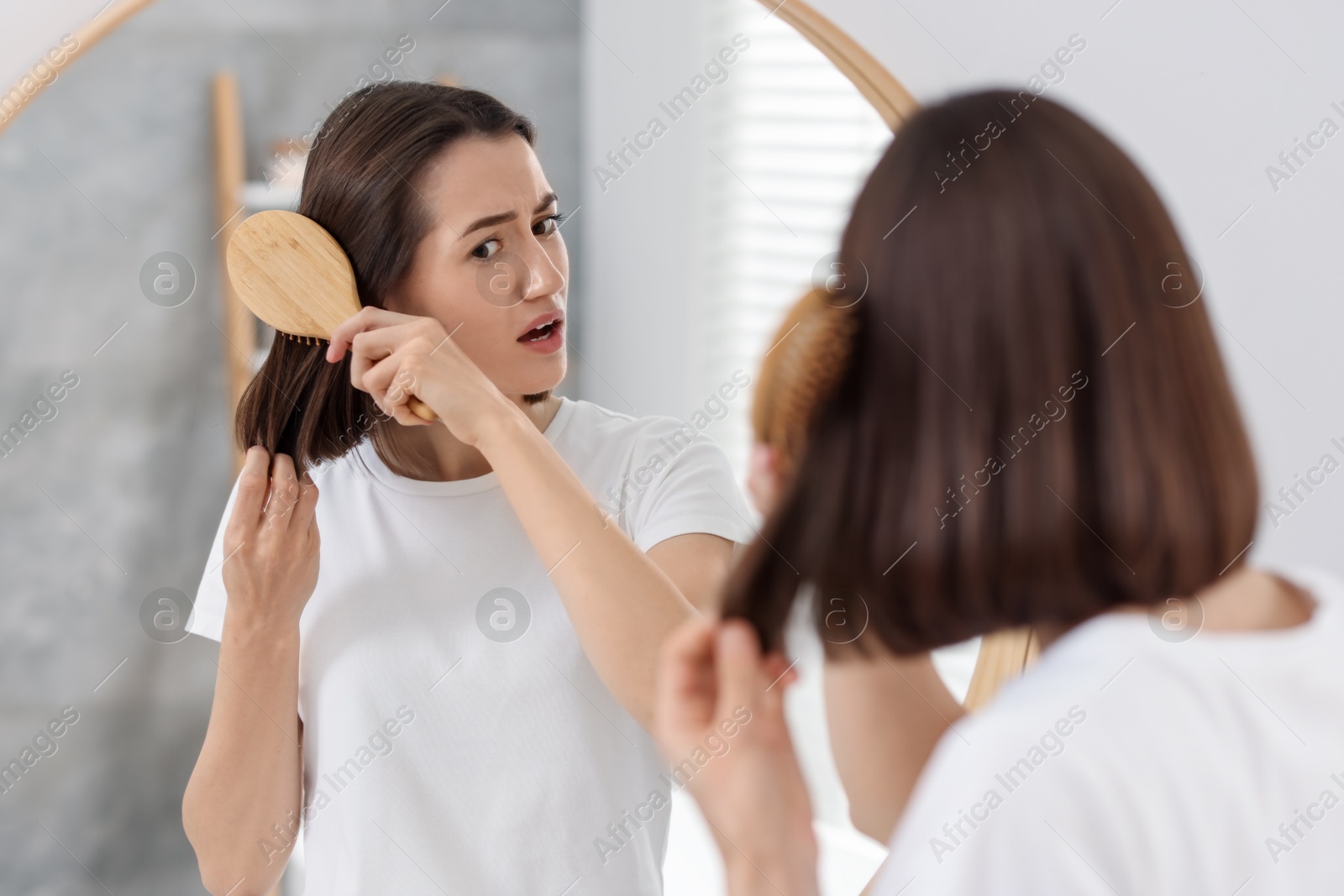 Photo of Stressed woman brushing her hair near mirror indoors. Alopecia problem