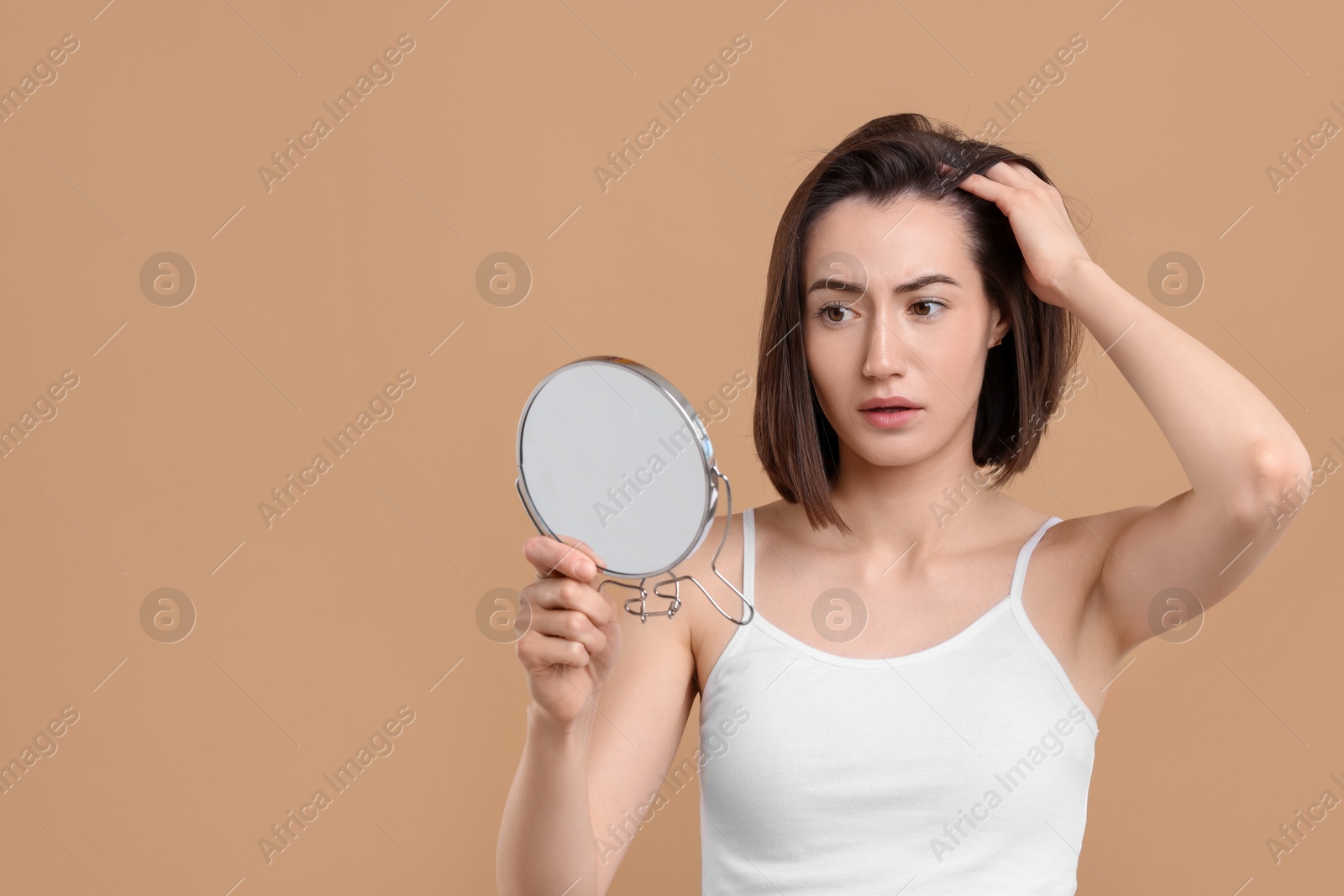 Photo of Sad woman with hair loss problem looking at mirror on light brown background. Space for text