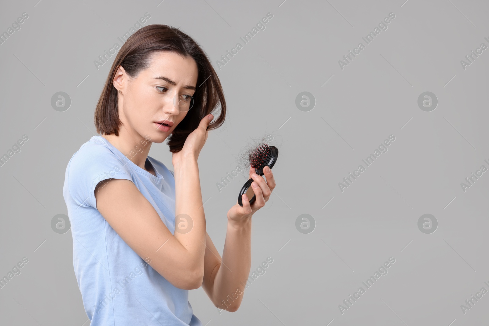 Photo of Stressed woman holding brush with lost hair on grey background, space for text. Alopecia problem