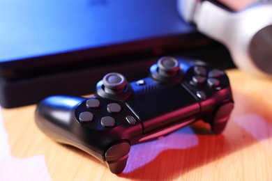 Video game console and wireless controller on wooden table, closeup