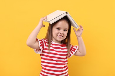Photo of Cute little girl with open book on orange background