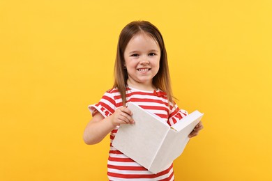 Photo of Cute little girl with open book on orange background