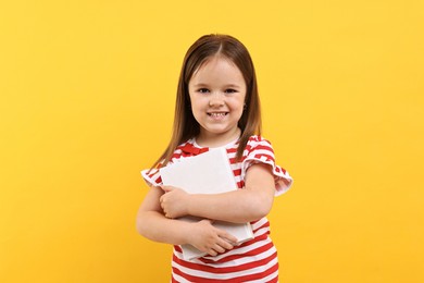 Cute little girl with book on orange background