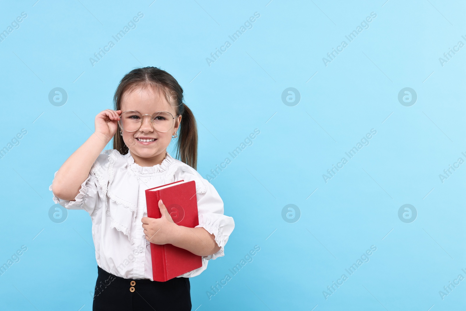 Photo of Cute little girl in glasses with book on light blue background. Space for text