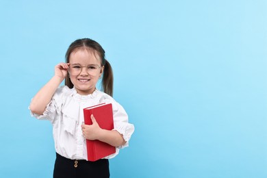 Cute little girl in glasses with book on light blue background. Space for text