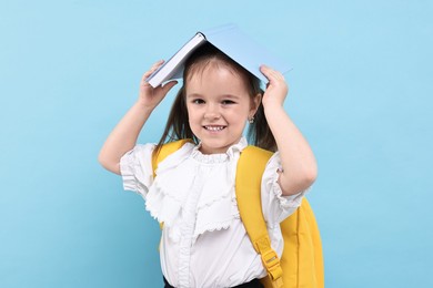 Photo of Cute little girl with open book and backpack on light blue background