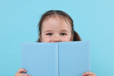 Photo of Cute little girl with open book on light blue background