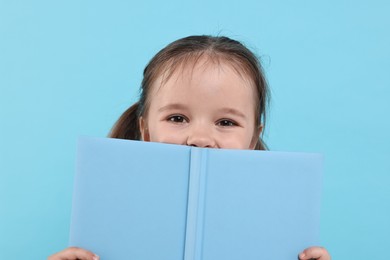 Cute little girl with open book on light blue background