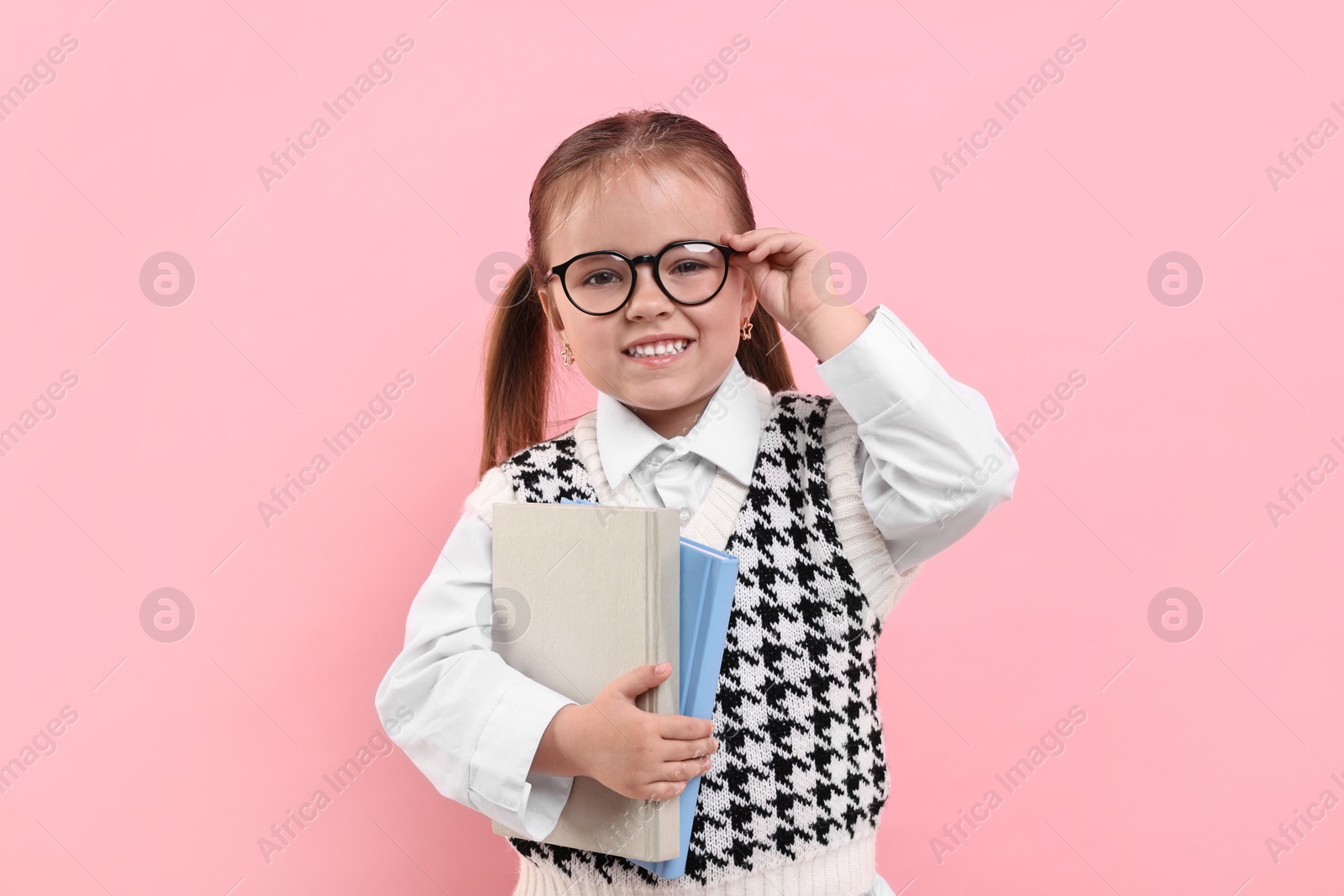 Photo of Cute little girl in glasses with books on pink background
