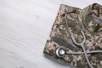 Stethoscope and military uniform on white wooden background, top view. Space for text