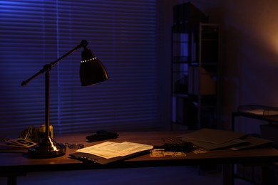 Detective workplace with documents and crime evidence on table at night