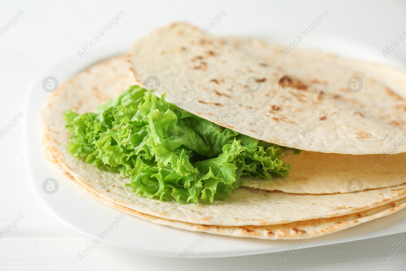 Photo of Tasty homemade tortillas and lettuce on white wooden table, closeup