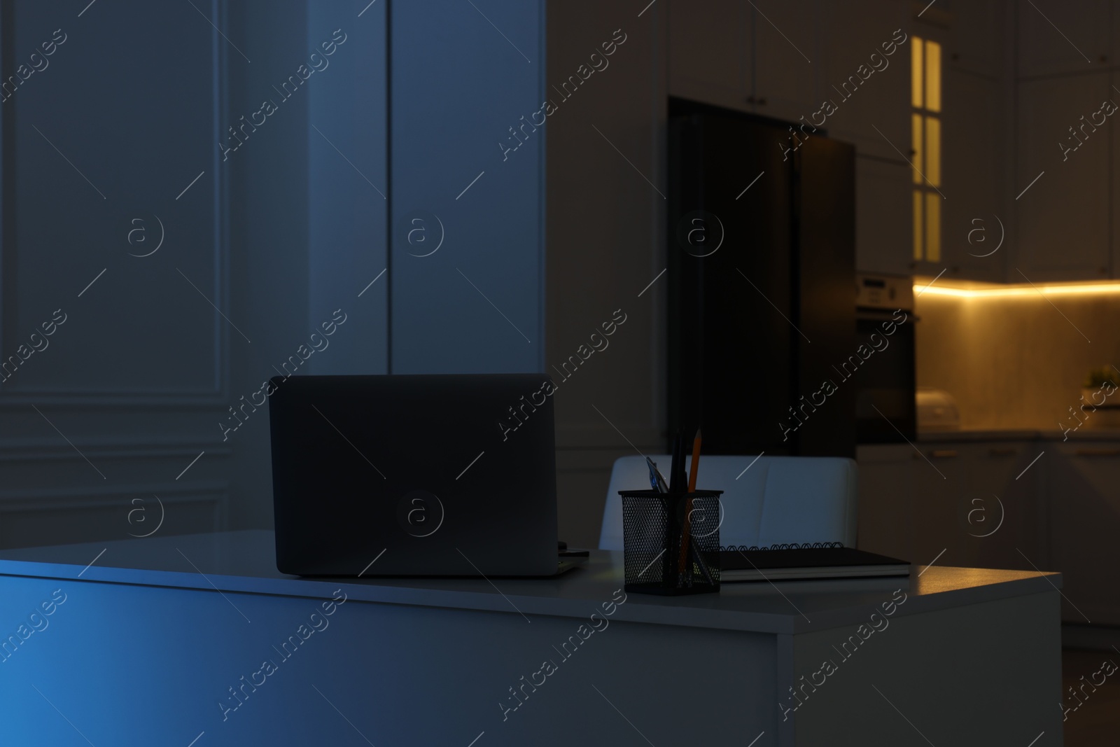 Photo of Cozy workplace with laptop and stationery on table in kitchen at night