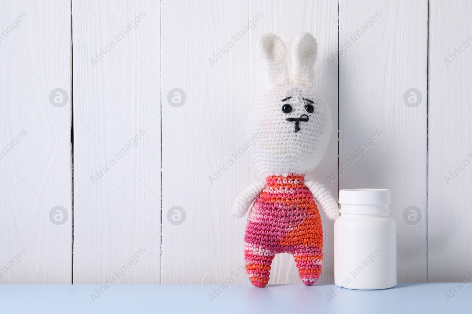 Photo of Toy bunny and bottle of pills on light blue table near white wooden wall, space for text