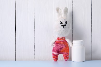 Toy bunny and bottle of pills on light blue table near white wooden wall, space for text