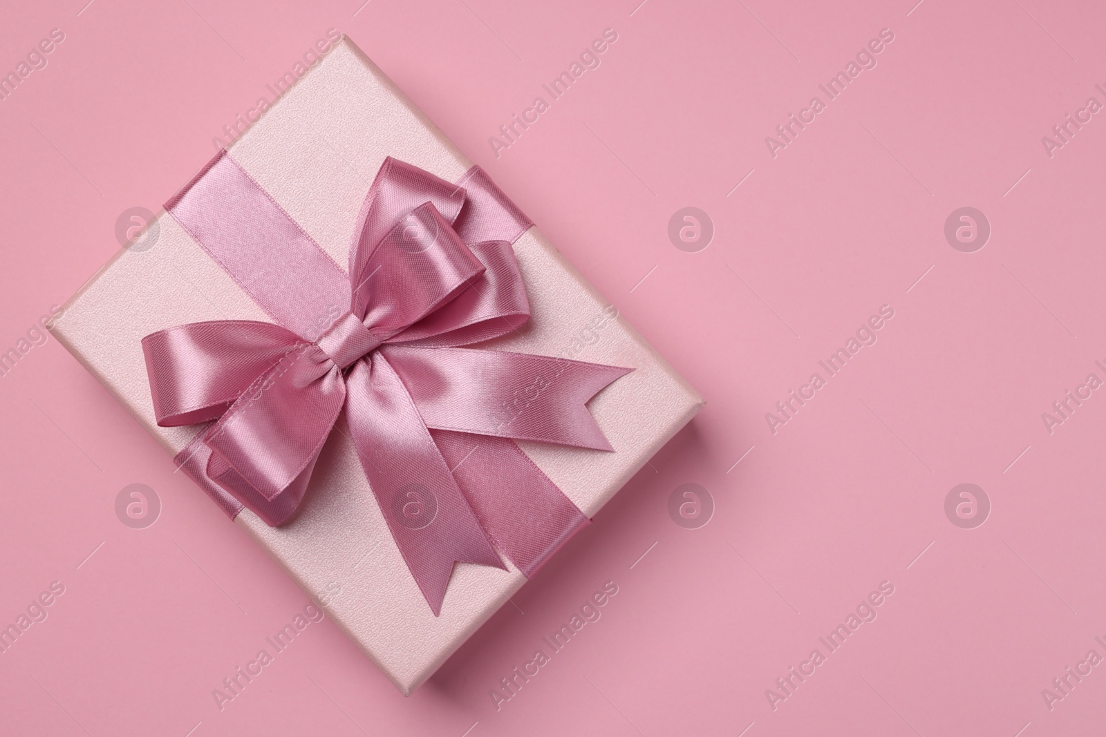 Photo of Beautiful gift box with color bow on pink background, top view. Space for text