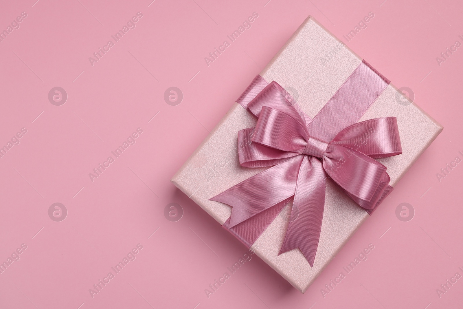 Photo of Beautiful gift box with color bow on pink background, top view. Space for text