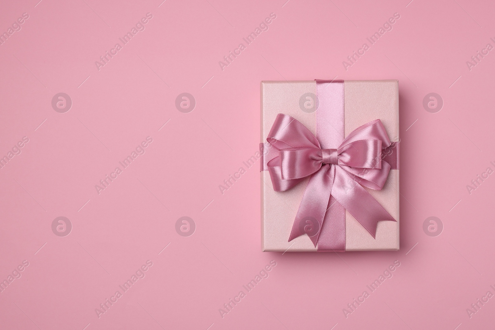 Photo of Beautiful gift box with color bow on pink background, top view. Space for text