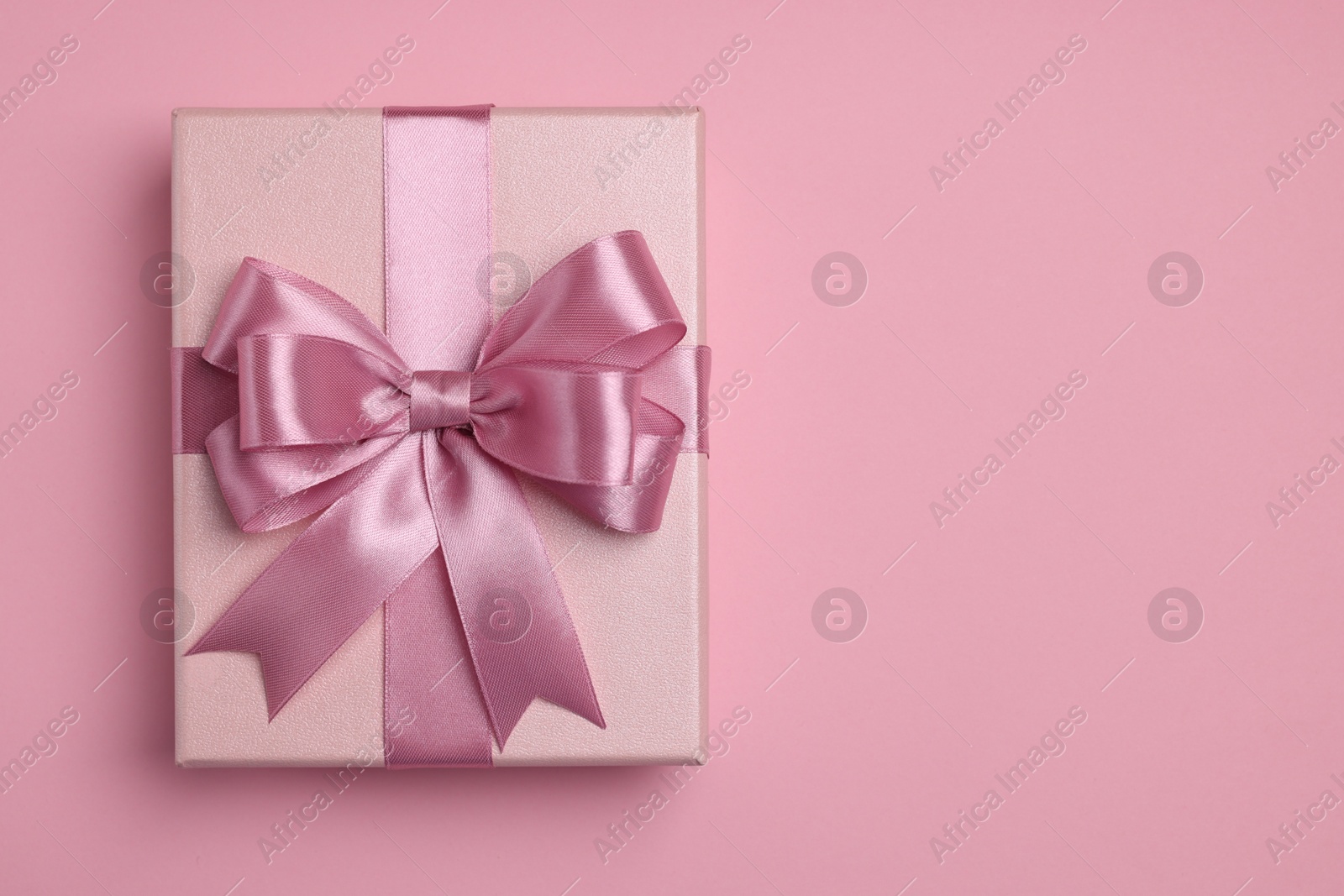 Photo of Beautiful gift box with color bow on pink background, top view. Space for text