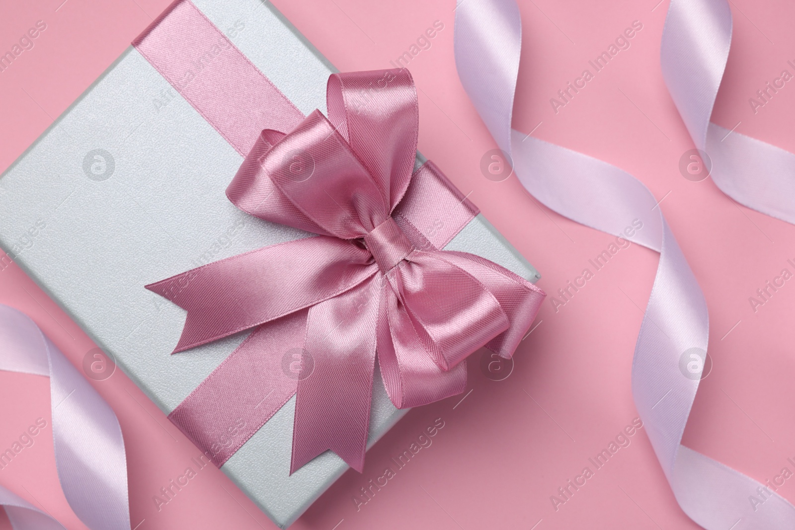 Photo of Beautiful gift box with color bow and ribbons on pink background, flat lay