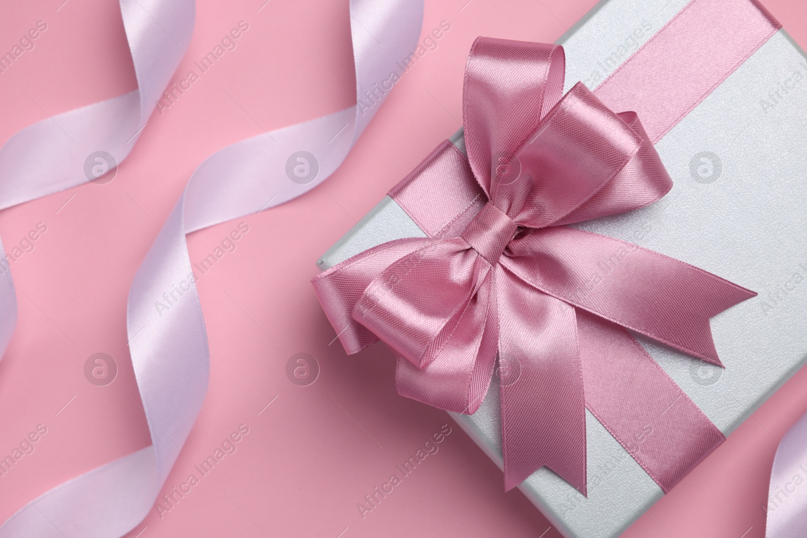 Photo of Beautiful gift box with color bow and ribbons on pink background, flat lay