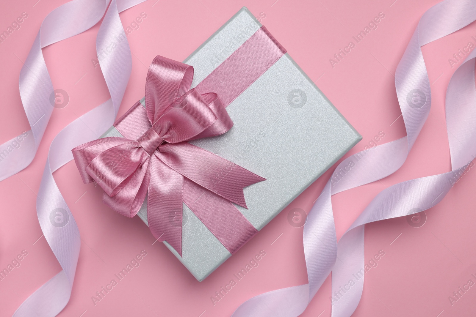 Photo of Beautiful gift box with color bow and ribbons on pink background, flat lay