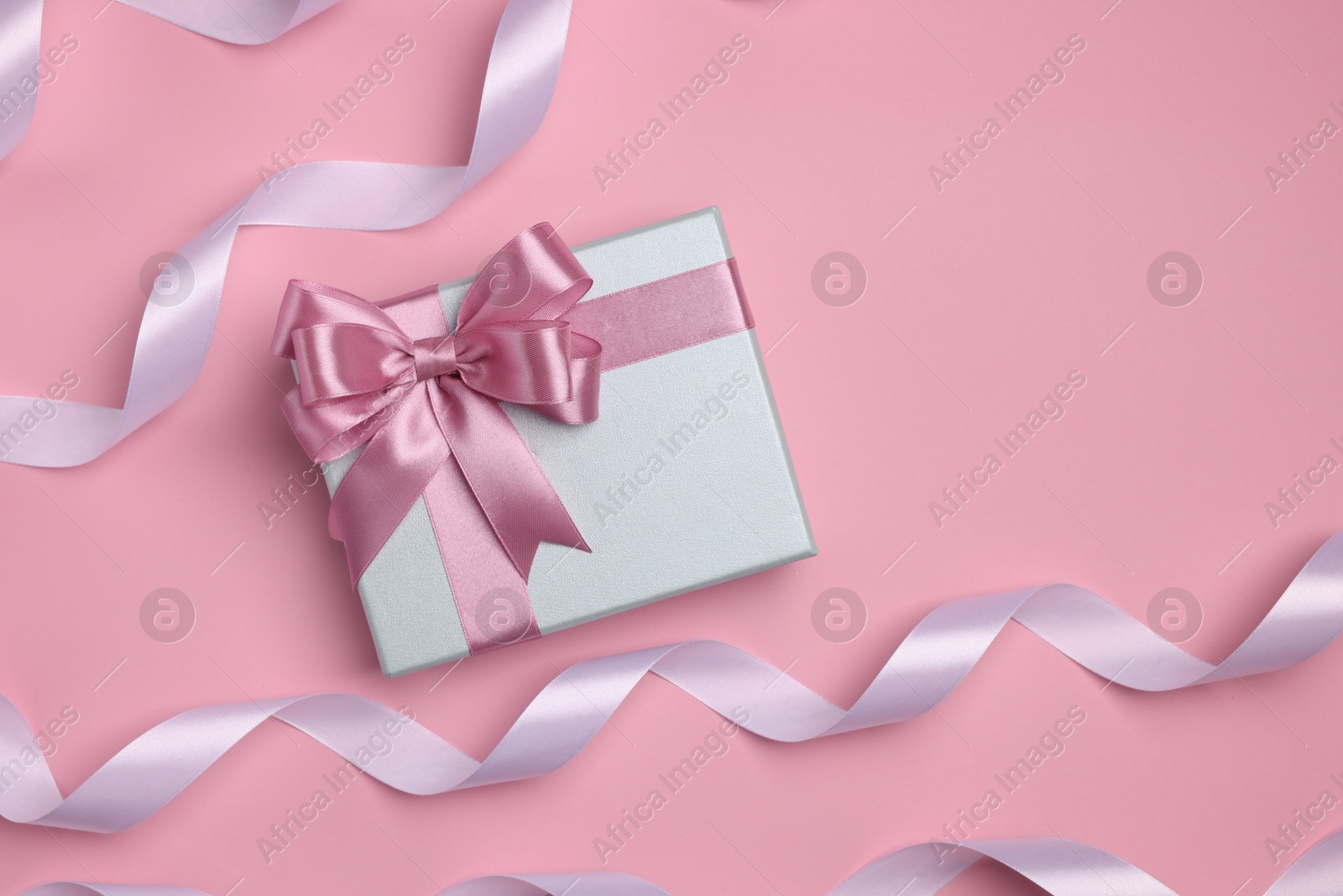 Photo of Beautiful gift box with color bow and ribbons on pink background, flat lay