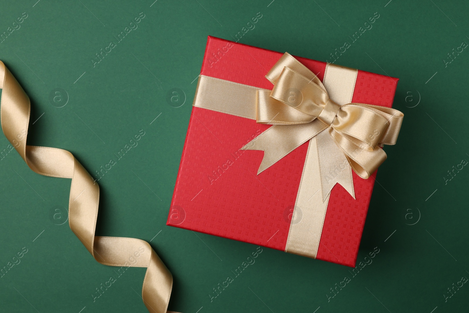 Photo of Beautiful red gift box with bow and ribbons on green background, flat lay