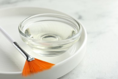 Photo of Bowl of chemical peel and brush on white table, closeup. Peeling procedure