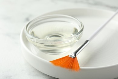 Bowl of chemical peel and brush on white table, closeup. Peeling procedure