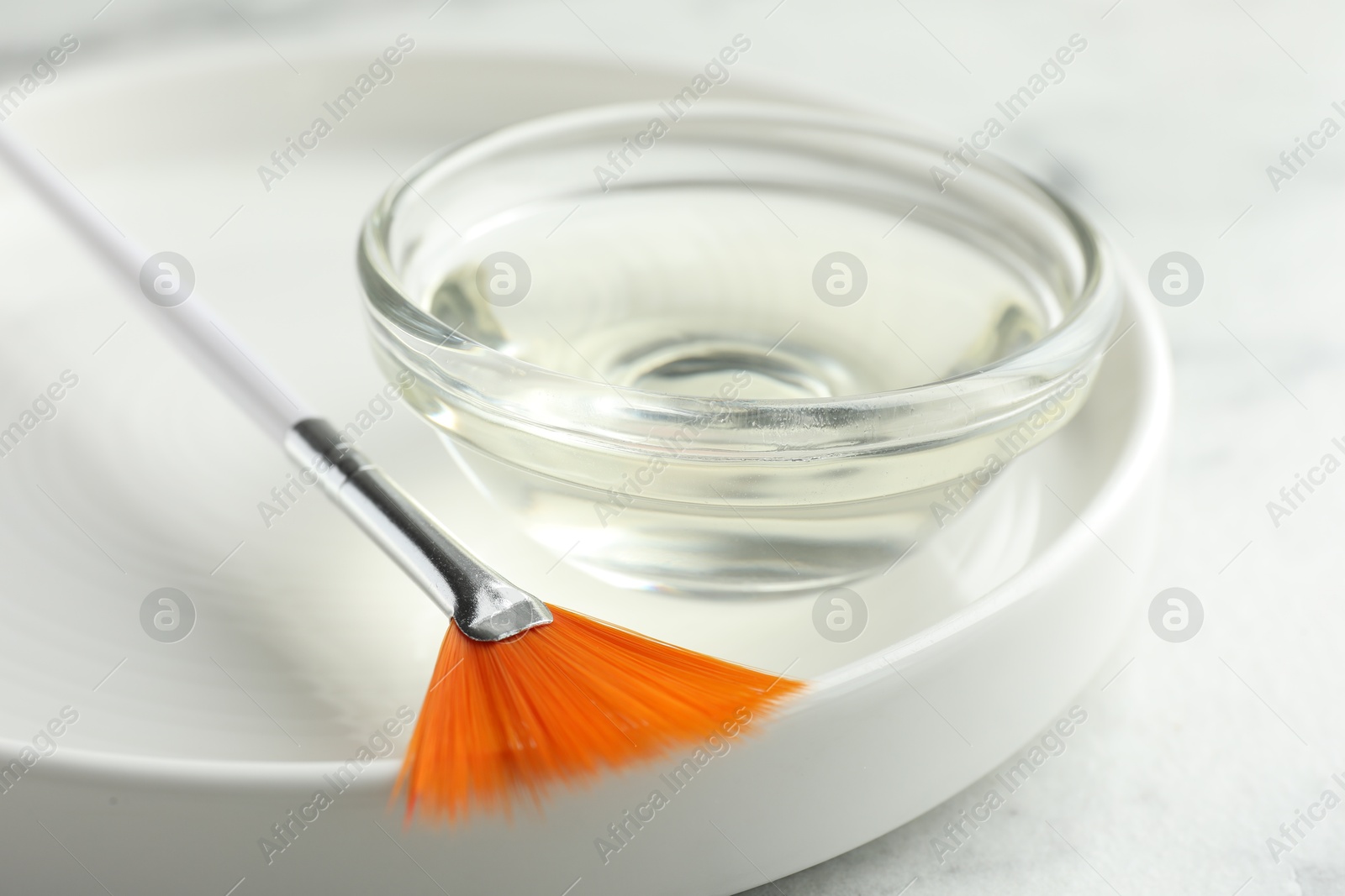 Photo of Bowl of chemical peel and brush on white table, closeup. Peeling procedure