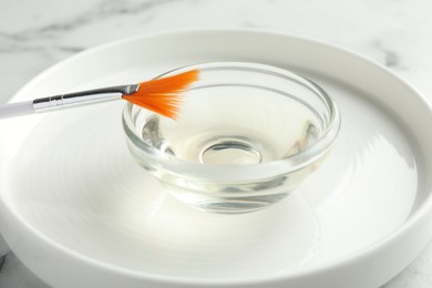 Photo of Bowl of chemical peel and brush on white table, closeup. Peeling procedure